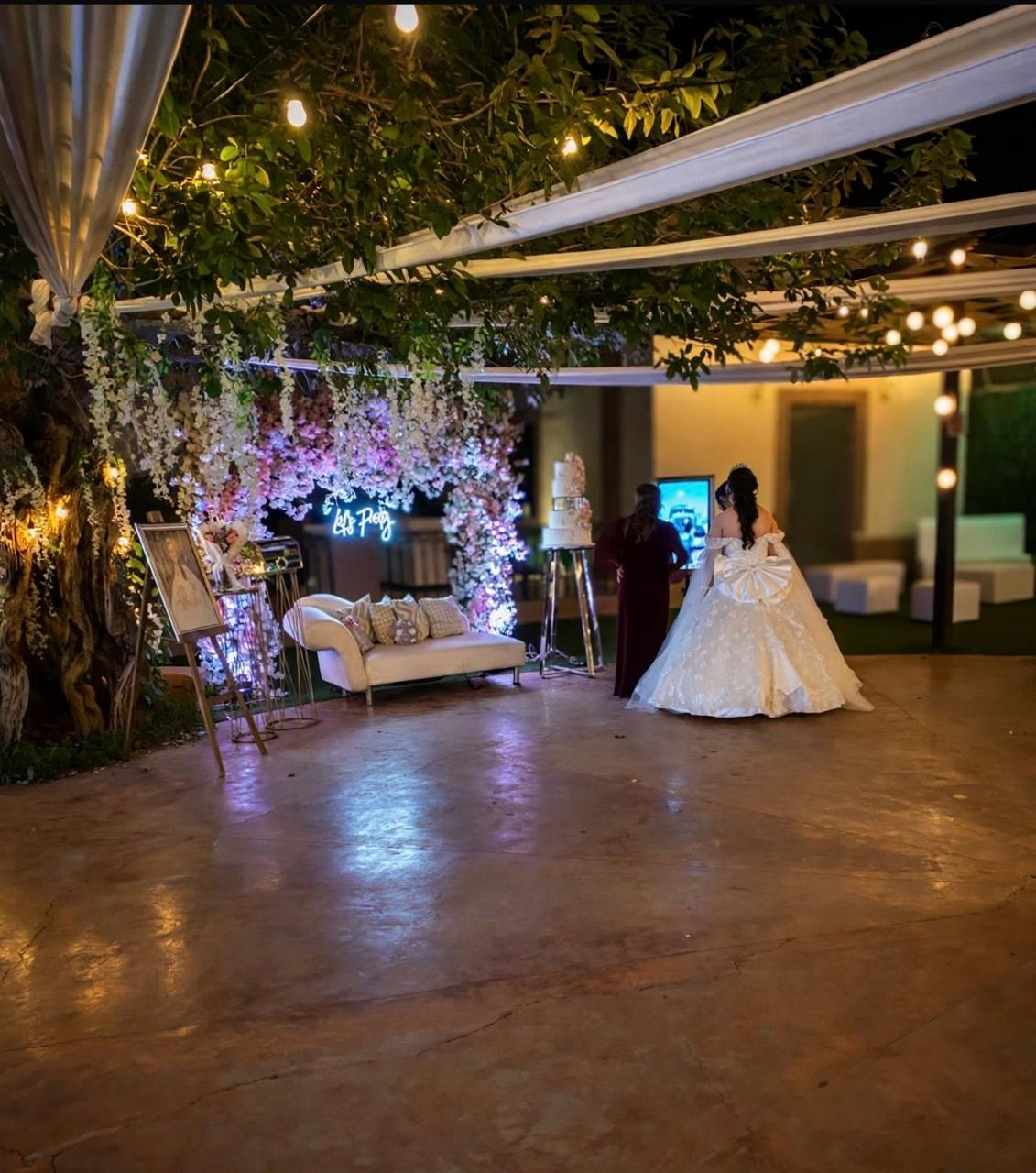Boda en La Casona: la novia bajo el arco de flores, con las series de luces y la terraza al fondo