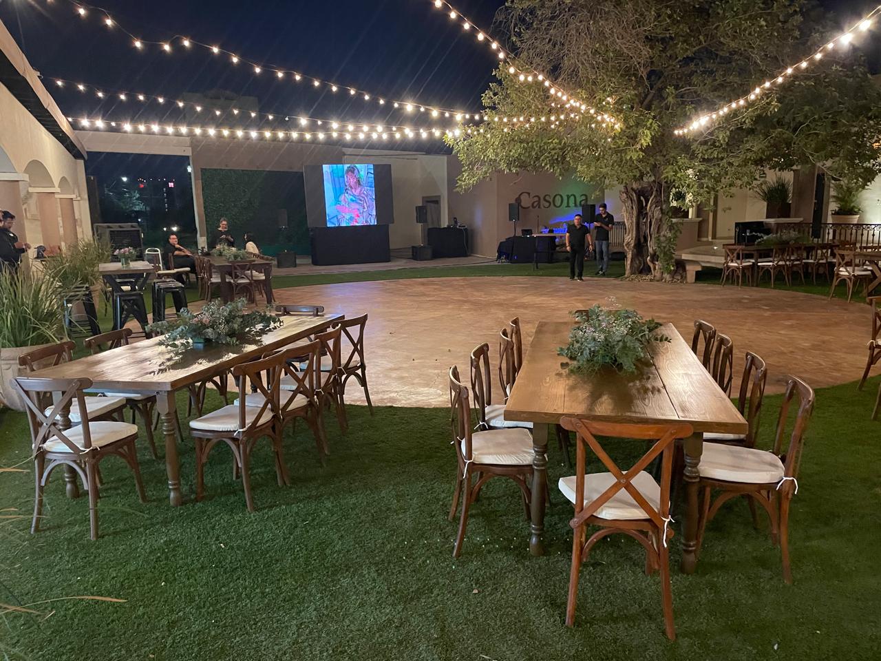 Mesas largas de madera sobre el pasto, con la pista y las series de luces de noche